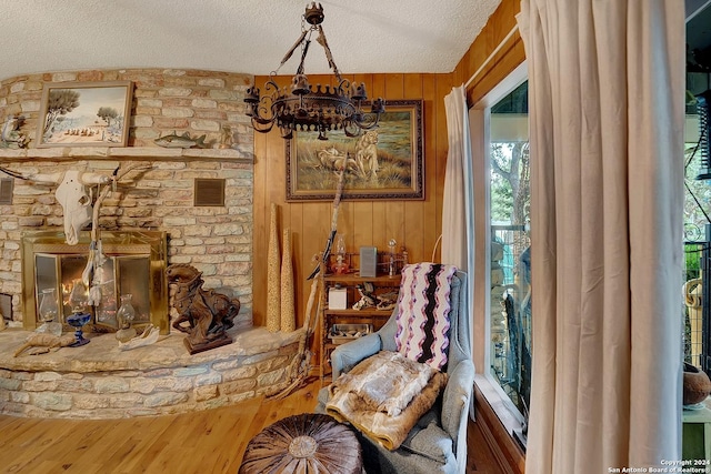 sitting room featuring visible vents, wood walls, a stone fireplace, a textured ceiling, and wood finished floors