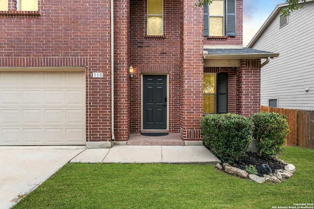 doorway to property featuring a garage, fence, and brick siding