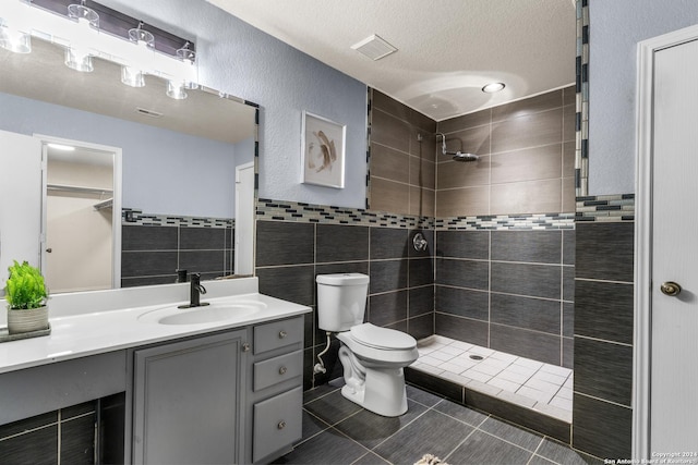 bathroom with visible vents, tile walls, toilet, a tile shower, and vanity