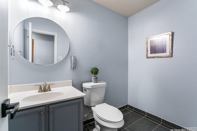 bathroom with vanity, baseboards, tile patterned flooring, toilet, and a textured wall