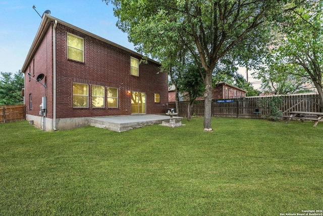 back of house featuring brick siding, a yard, a patio, and a fenced backyard