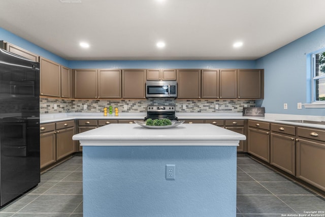 kitchen featuring backsplash, a center island, dark tile patterned floors, light countertops, and stainless steel appliances