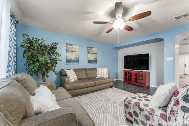 tiled living area with a ceiling fan, arched walkways, visible vents, and baseboards