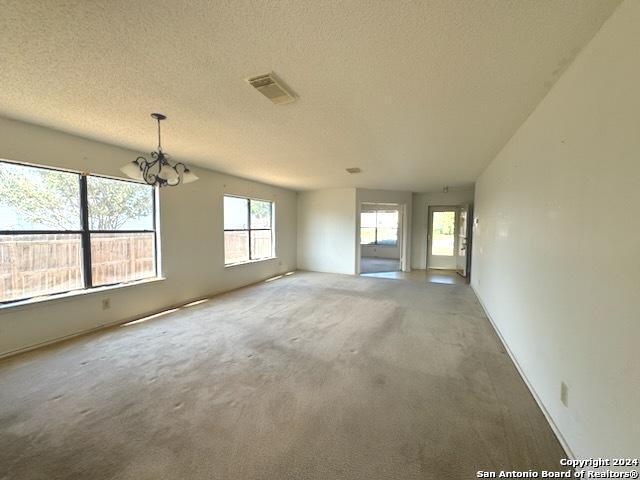 empty room featuring a notable chandelier, visible vents, carpet floors, and a textured ceiling