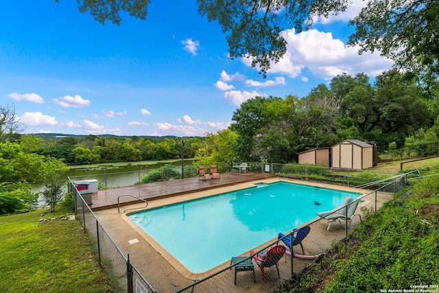 view of pool featuring a water view, a yard, and a storage unit