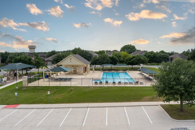 pool at dusk featuring fence, a patio, a community pool, and a lawn