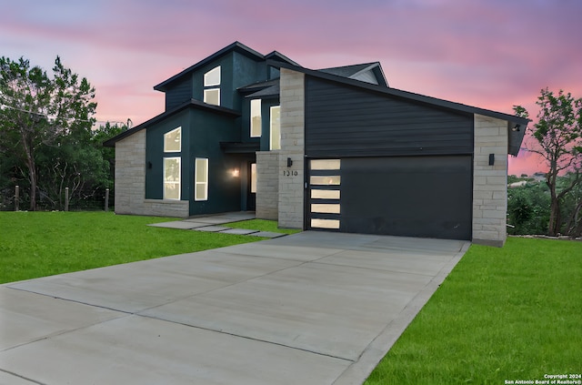 contemporary house featuring an attached garage, concrete driveway, a front lawn, and stone siding