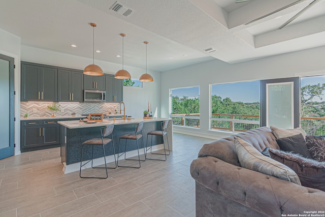 kitchen with visible vents, decorative backsplash, stainless steel microwave, open floor plan, and light countertops