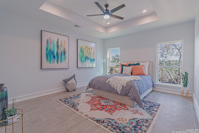 bedroom featuring a tray ceiling, multiple windows, visible vents, and baseboards