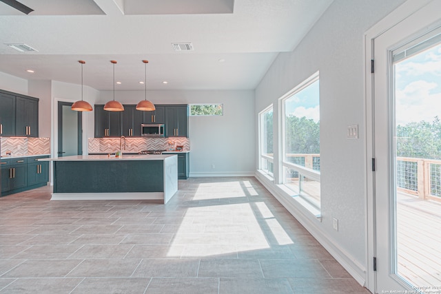 kitchen featuring an island with sink, pendant lighting, sink, and decorative backsplash