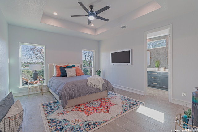 bedroom featuring a tray ceiling, recessed lighting, visible vents, ensuite bathroom, and baseboards