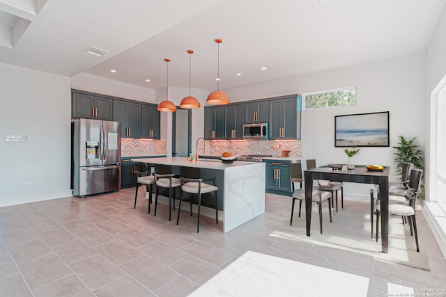 kitchen with backsplash, appliances with stainless steel finishes, an island with sink, hanging light fixtures, and sink