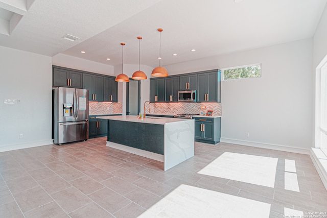 kitchen with decorative light fixtures, appliances with stainless steel finishes, sink, decorative backsplash, and a center island with sink