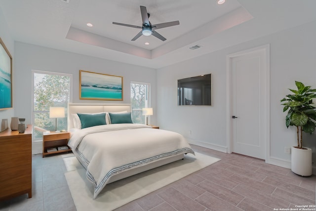 bedroom with multiple windows, ceiling fan, and a raised ceiling