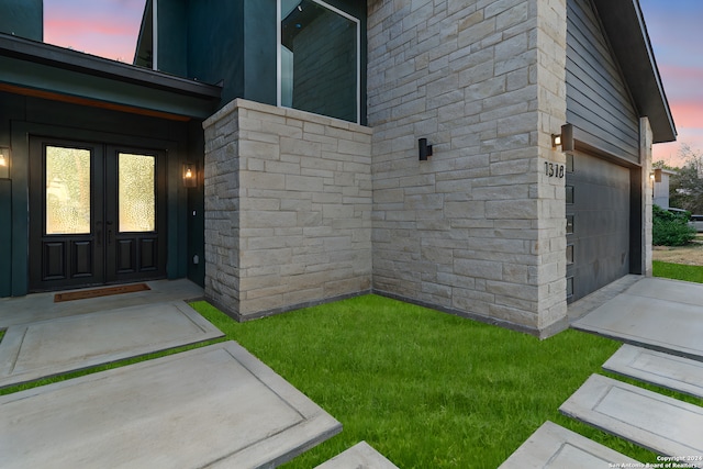 exterior entry at dusk with a garage, a lawn, french doors, and brick siding