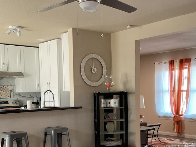 kitchen featuring stainless steel electric range oven, backsplash, white cabinetry, ceiling fan, and under cabinet range hood