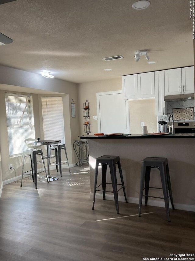 kitchen with a breakfast bar, hardwood / wood-style floors, a textured ceiling, and white cabinets