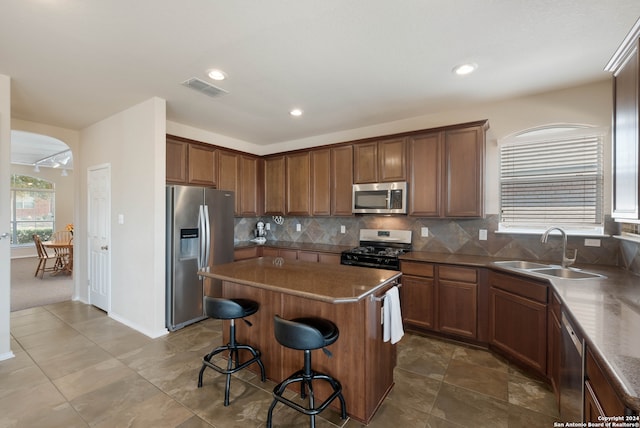 kitchen with appliances with stainless steel finishes, sink, a kitchen island, decorative backsplash, and a breakfast bar