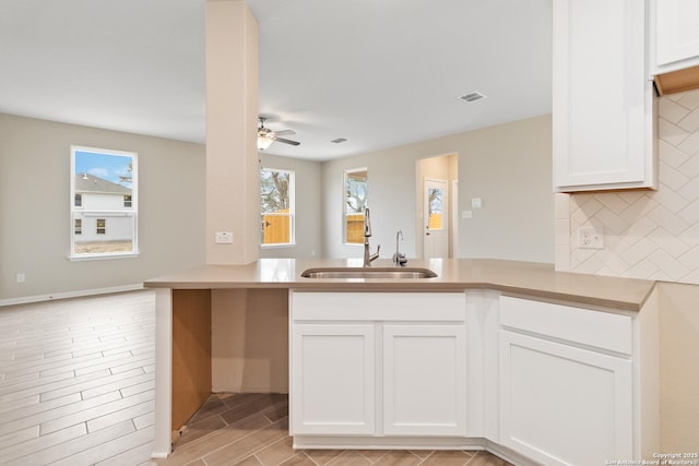 kitchen featuring visible vents, backsplash, a sink, ceiling fan, and a peninsula