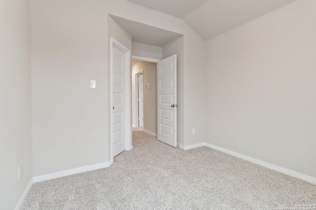 spare room featuring lofted ceiling, baseboards, and light colored carpet