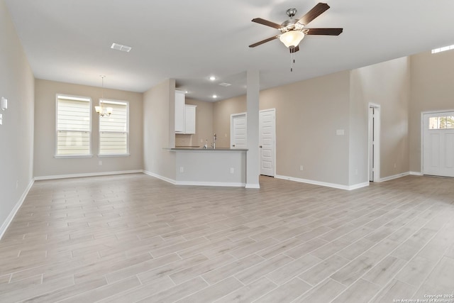 unfurnished living room featuring a wealth of natural light, baseboards, light wood finished floors, and ceiling fan with notable chandelier