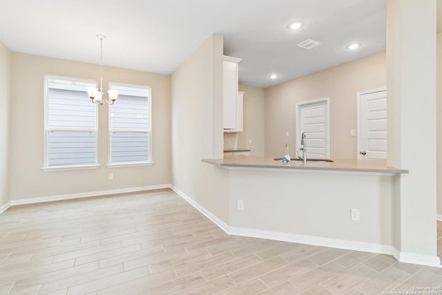 kitchen featuring a peninsula, a sink, visible vents, and white cabinetry