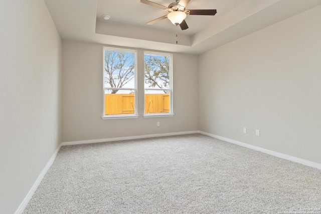 carpeted empty room featuring a tray ceiling, ceiling fan, and baseboards