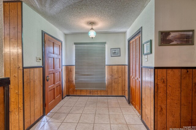 foyer featuring wooden walls, light tile patterned flooring, and a textured ceiling