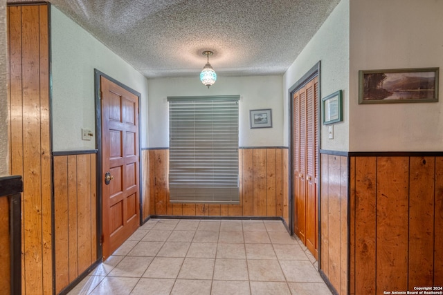 interior space featuring a wainscoted wall, wood walls, a textured ceiling, and light tile patterned floors