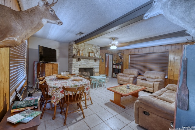 living room featuring a fireplace, wooden walls, a textured ceiling, light tile patterned floors, and ceiling fan