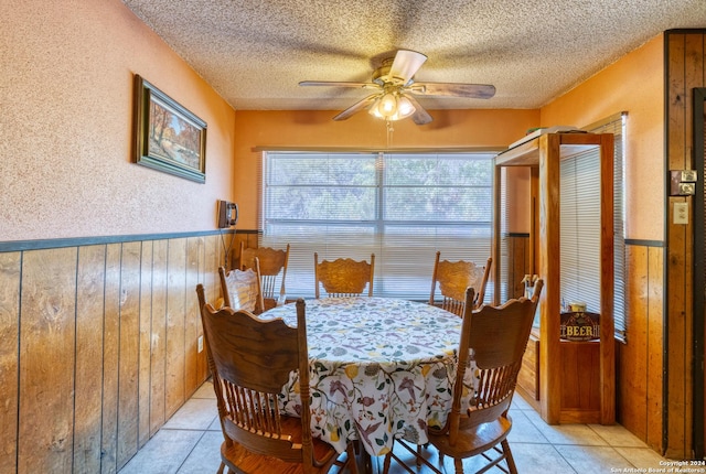 dining space with a ceiling fan, a wainscoted wall, wooden walls, and a textured ceiling