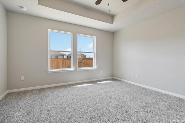 carpeted spare room featuring a raised ceiling, a ceiling fan, and baseboards