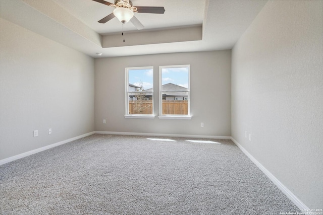 carpeted spare room featuring ceiling fan, a raised ceiling, and baseboards