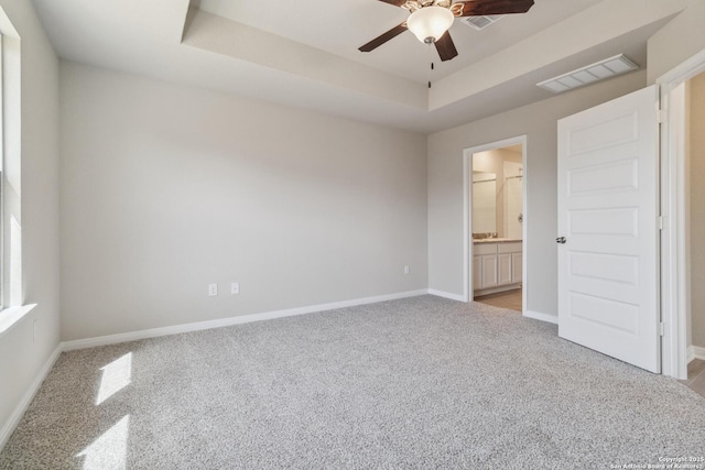 unfurnished bedroom with connected bathroom, light colored carpet, visible vents, baseboards, and a tray ceiling