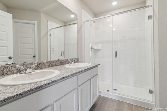 bathroom featuring a stall shower, double vanity, a sink, and wood finished floors