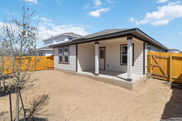 rear view of property featuring a gate, fence, and a patio