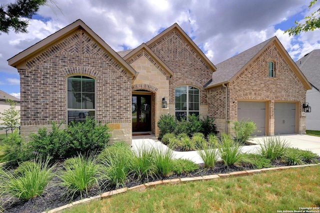 french country home with stone siding, brick siding, driveway, and roof with shingles