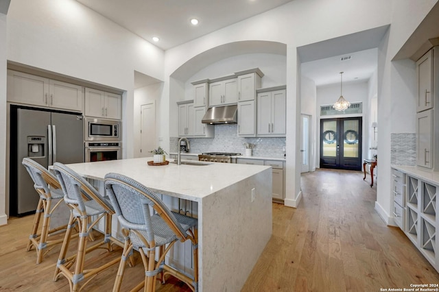 kitchen featuring backsplash, appliances with stainless steel finishes, light hardwood / wood-style floors, sink, and a center island with sink