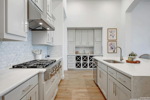 kitchen featuring a kitchen island with sink, backsplash, sink, appliances with stainless steel finishes, and light hardwood / wood-style floors