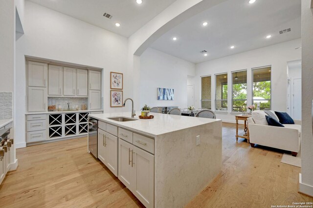 kitchen with a kitchen island with sink, light wood-type flooring, sink, and decorative backsplash