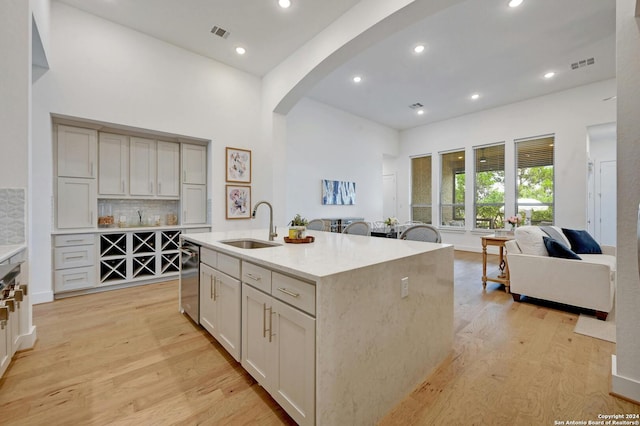 kitchen featuring arched walkways, light wood finished floors, visible vents, open floor plan, and a sink