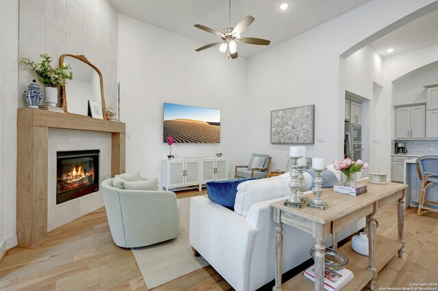 living room with light wood-type flooring, ceiling fan, high vaulted ceiling, and a tiled fireplace