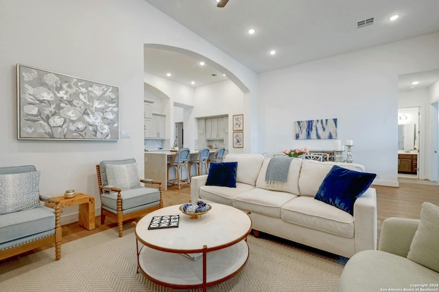 living area with light wood finished floors, visible vents, arched walkways, high vaulted ceiling, and recessed lighting