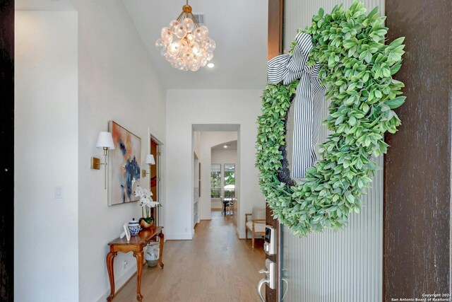 foyer entrance featuring vaulted ceiling, hardwood / wood-style floors, and an inviting chandelier