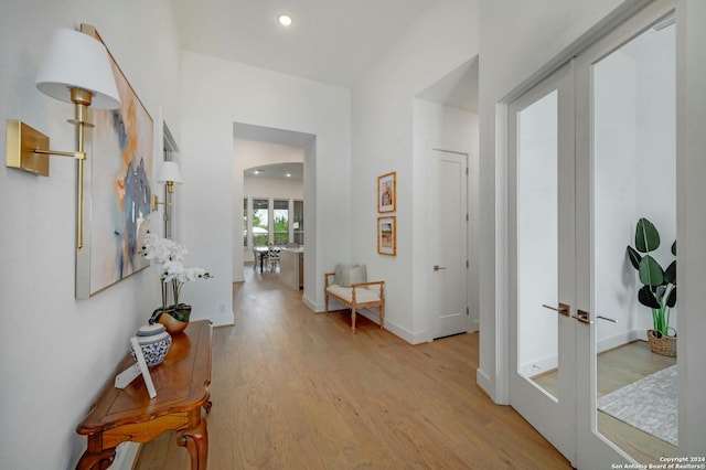 hall featuring light wood-style flooring, arched walkways, baseboards, and french doors