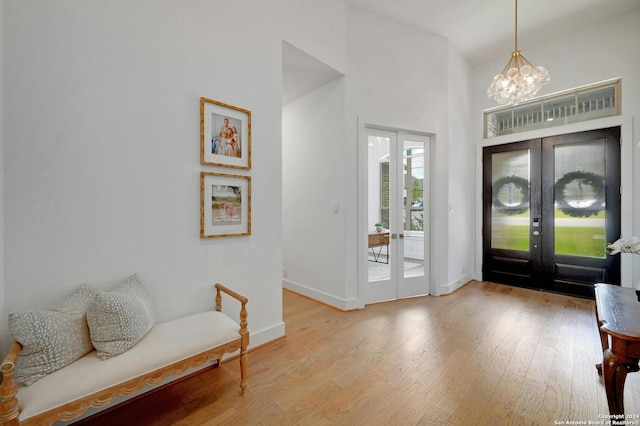 entrance foyer featuring a notable chandelier, a high ceiling, wood finished floors, baseboards, and french doors