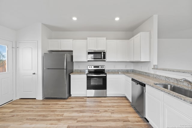 kitchen with light stone counters, stainless steel appliances, light hardwood / wood-style floors, white cabinetry, and sink