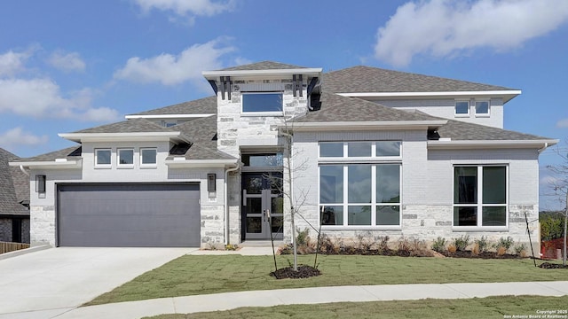 prairie-style house with stone siding, roof with shingles, concrete driveway, and a front yard