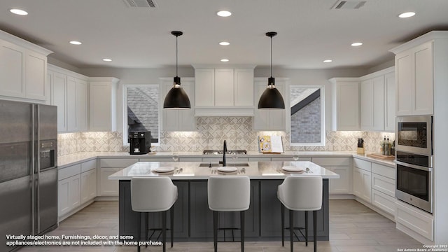 kitchen with light countertops, visible vents, appliances with stainless steel finishes, a kitchen island with sink, and white cabinets