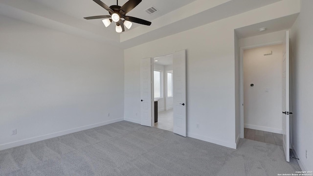 unfurnished bedroom with ceiling fan, a tray ceiling, and light carpet